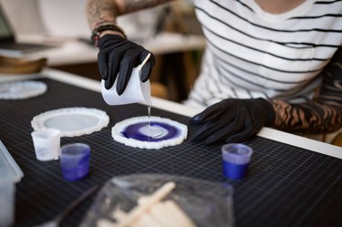 Craft woman pouring epoxy in the silicone mold, while working from her home workshop