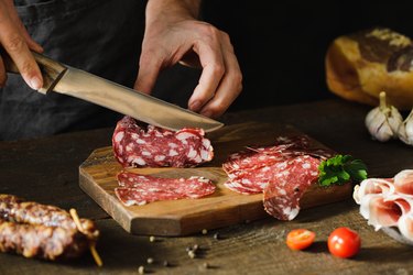 Woman's hands cutting salami on a wooden cutting board