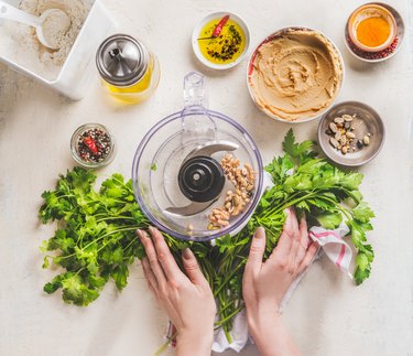 Women hands holding ingredients for healthy gluten free chips bread oder falafel bread with fresh herbs, , Chickpeas hummus , nuts and olive oil on white kitchen table