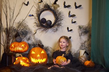 Halloween Child with pumpkin in hands in interior house. Blonde on web and bat.