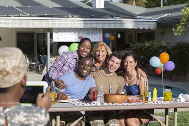 Boy photographing male soldier with family and friends at homecoming party