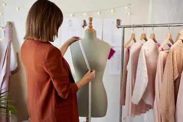 Female fashion entrepreneur measuring dressmaker's model by clothes rack at design studio
