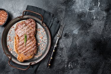 Barbecue Grilled striploin or New York  beef meat steak with pink salt and herbs. Black background. Top view. Copy space