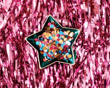 Multicolored glittery confetti are in a festive star-shaped plate. The background is made of tinsel.