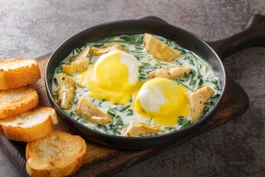 Eggs Sardou New Orleans brunch recipe made with poached eggs, served artichoke and creamed spinach and topped with Hollandaise sauce close up in the plate. Horizontal