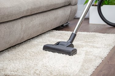 A woman vacuums a gray carpet with a vacuum cleaner. Cleaning and cleanliness concept