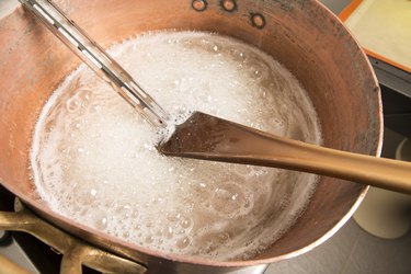 boiling syrup of sugar in copper pan with thermometer and big spoon