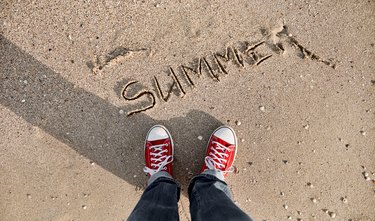 In the photo taken from above, the inscription of the word summer on wet sand washed by the sea wave