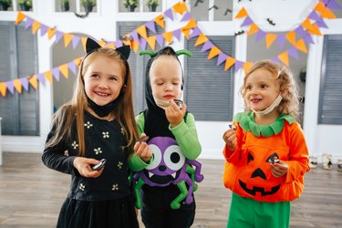 Children in Halloween costumes and with masks on are playing trick or treat and laughing.