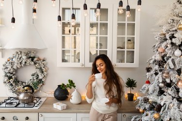 Young woman enjoying coffee while standing at kitchen in Christmas morning.