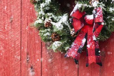 Christmas wreath with plaid bow on red barn while it snows