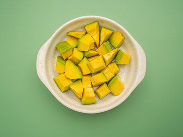 Top view of diced avocados in a ceramic bowl on a green background