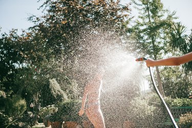 teenagers having fun splashing water from hose in backyard