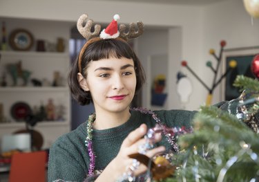 Young woman is decorating christmas tree in livingroom.