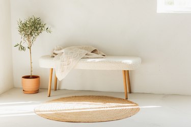 Fluffy fur bench, wicker rug and olive plant in ceramic vase.