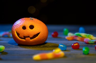 An orange disguised  as a pumpkin surrounded by candies on Halloween night