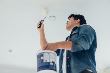 Young Man Painting The Ceiling With A Paint Roller At Home