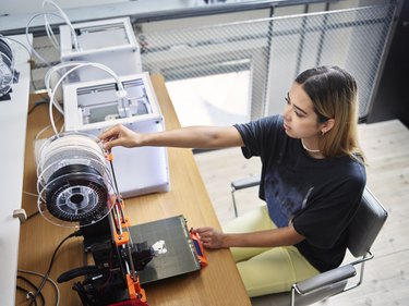 Young technician adjusting filament roll on 3d printer at workshop
