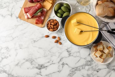 Pot of tasty cheese fondue and snacks on white marble table
