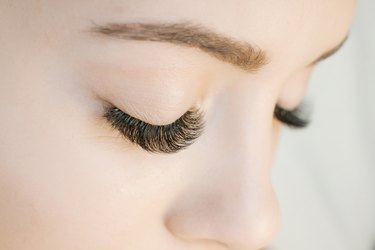 Eyelash extension procedure. Close up view of beautiful woman eyes with long eyelashes. Lengthening lashes for girl in a beauty salon. Beauty concept.