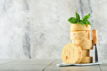 Cheeses stacked on serving board with basil and knife