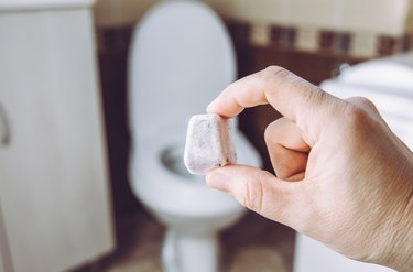 DIY toilet fizzie bomb for cleaning home toilet bowl. Selective focus on woman hand, holding homemade natural cleaning pod tablet. Green sustainable lifestyle concept.