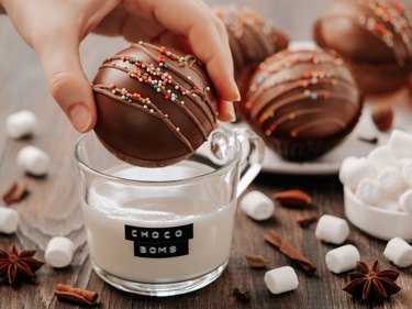 Chocolate cocoa bomb or ball in hand near milk cup