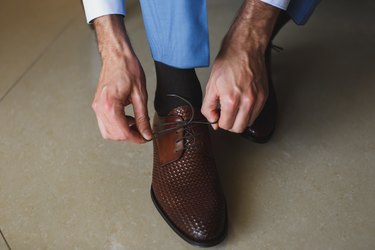 Man's hands tying shoelace of his new shoes. People, business, fashion and footwear concept - close up of man leg and hands tying shoe laces.