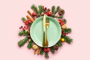 Plate, winter fir branches, cones and Christmas decoration on pink background