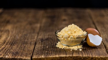 Portion of powdered eggs in clear bowl, alongside broken egg shell