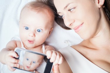 Happy mother with a baby lying on a white bed