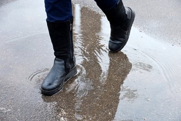 Rain in city, female legs in boots on a street with puddles