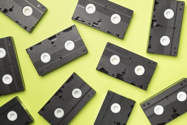 Old VHS cassette tapes scattered on color background, top view