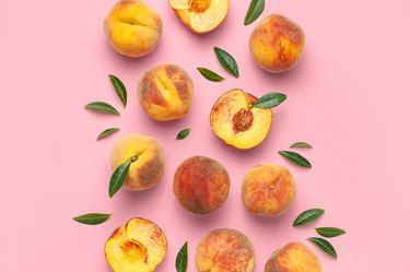 Ripe juicy peaches with green leaves on pink background
