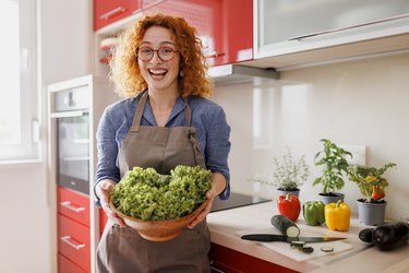 Young beautiful woman making salad in her red kitchen