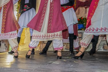 Cropped view of Greek dancers on stage in beautiful embroidered costume with women in front of men - legs and feet - movement blur