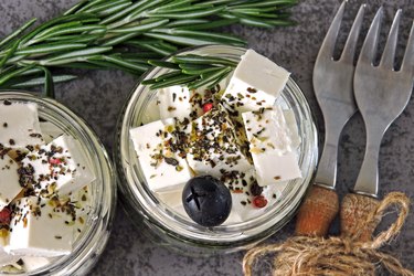 Pieces of feta and olives in jars with rosemary and spices.