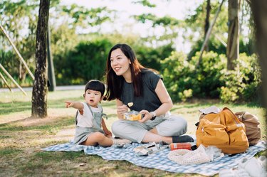 Young Asian mother and cute little daughter enjoying family bonding time having a picnic on a beautiful day in park