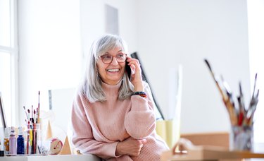 Senior woman indoors in art painting class, using telephone.