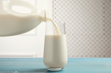 Pouring milk from gallon bottle into glass on blue wooden table