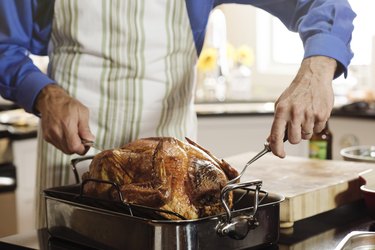 Senior man carving turkey in kitchen at home during Thanksgiving