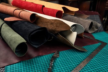 Rolled up samples of textures of genuine leather of different colors on a leather background, on a table with mats and tools for cutting pieces of leather