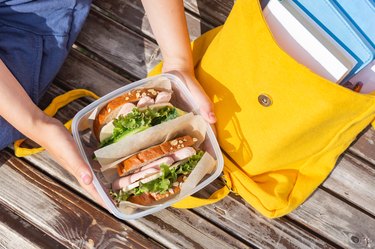 Lunch box in the hands of a child. Sandwiches  in a plastic container. Snack, school breakfast. Back to school. Lunch break.Yellow backpack with books