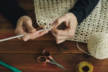 A woman is crocheting a blanket on a wooden table