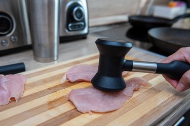 female hands beat chicken fillet with a hammer