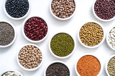 Dried legumes assorted in many bowls on white as lentils, chickpeas, soybeans and beans