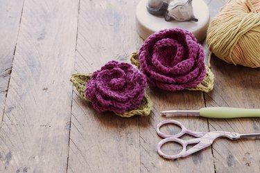 Handmade crocheted flowers, crochet hook, scissors and ball of wool in rustic wooden background. Selective focus and copy space