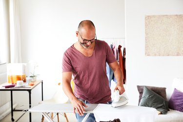 portrait of a content mature adult man ironing a shirt at home