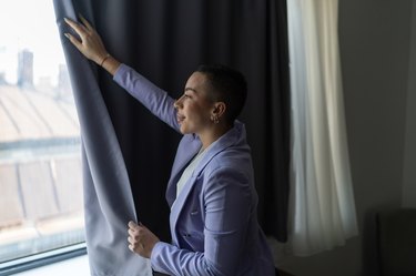 Businesswoman standing in apartment and opening curtain
