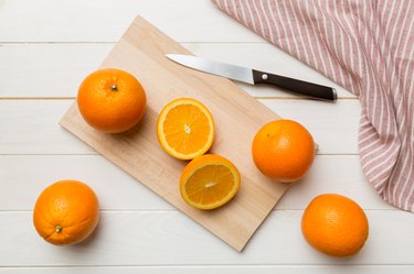 Fresh ripe oranges with knife on cutting board on table